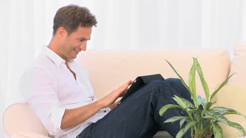 Smiling Man Using Tablet While Relaxing on Sofa