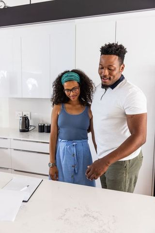 Diverse couple reviewing documents at modern marble kitchen counter for home planning
