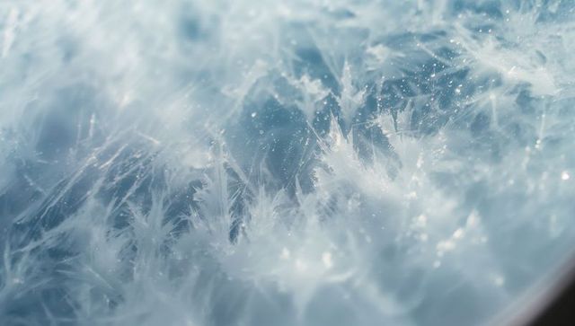 Delicate frost patterns on ice crystals forming on glass surface