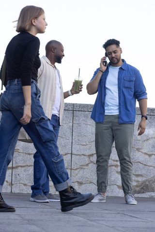 Friends walking and talking on phone by stone railing holding green smoothie