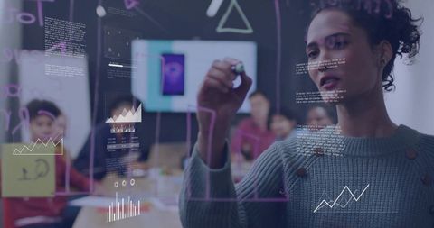 Woman sketching data visualizations on glass board during collaborative brainstorming