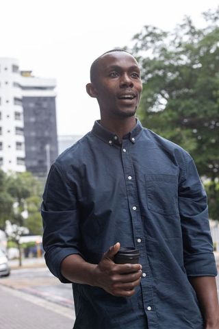 African professional walking with takeaway coffee on urban sidewalk in navy shirt