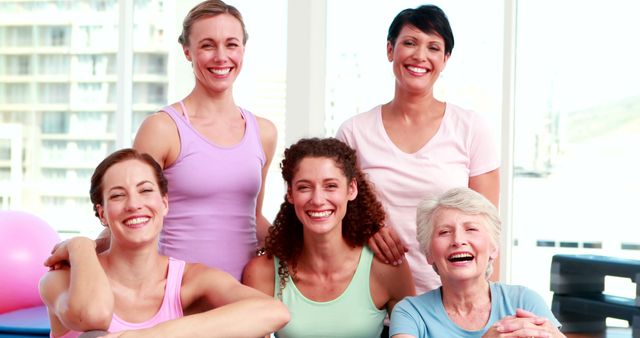 This image shows a group of smiling women of various ages relaxing together in a bright, indoor setting. They appear to be bonding, possibly after a fitness session. Suitable for content focusing on health, wellness, diverse communities, mature groups, or social activities for women.