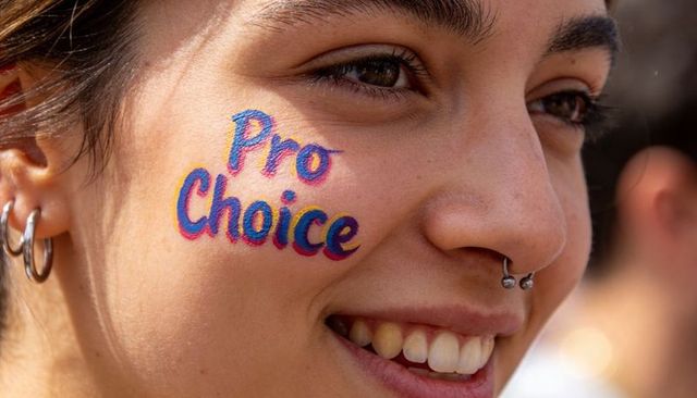 Smiling woman showing pro choice face paint on cheek at outdoor rally with septum piercing
