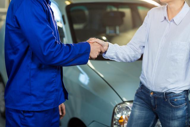 Mid-section of customer shaking hands with mechanic in repair garage