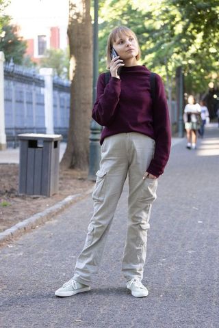 Young woman standing on campus pathway talking on smartphone wearing burgundy sweater