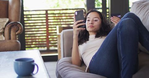 Young Woman Reclined on Sofa Browsing Smartphone