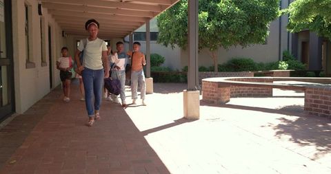 Diverse teens walking sunlit school courtyard brick walkway african american teen leading