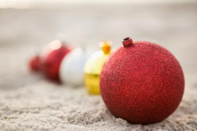 Red and other Christmas baubles lined up on sandy beach. Perfect for holiday travel promotions, tropical celebrations, and beach-themed holiday greeting cards.