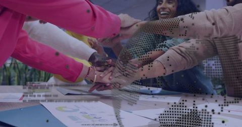 Joining hands around meeting table with digital network overlay and business reports