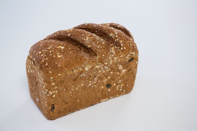 Close-up of a fresh whole grain bread loaf with seeds on a white background. Ideal for use in food blogs, bakery advertisements, healthy eating promotions, and diet-related content.