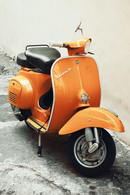 Orange Vespa scooter is parked on a concrete street, with its iconic design shining through. Ideal for themes related to transportation, vintage aesthetics, urban exploration, and retro design. This can be used in blogs about motorcycle culture, travel guides, advertisements for Vespa, or decor inspiration.
