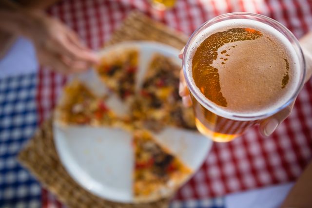 Cropped hand of woman holding beer glass over pizza plate
