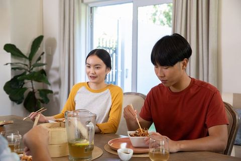 Asian Couple Enjoying Leisurely Meal with Noodles and Chopsticks at Dining Table
