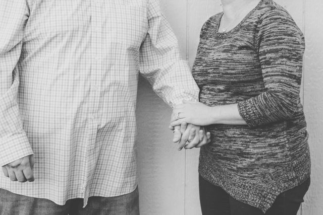 This image shows a senior couple standing indoors and holding hands. It is in grayscale, which adds a timeless and nostalgic feel. This image can be used to depict themes of love, companionship, and support among elderly individuals. It is ideal for use in articles, blog posts, and advertisements focusing on senior care, family relations, and intimacy in later life.