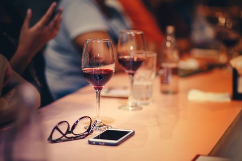 Red wine glasses resting on bar with smartphone and reading glasses creating cozy evening scene