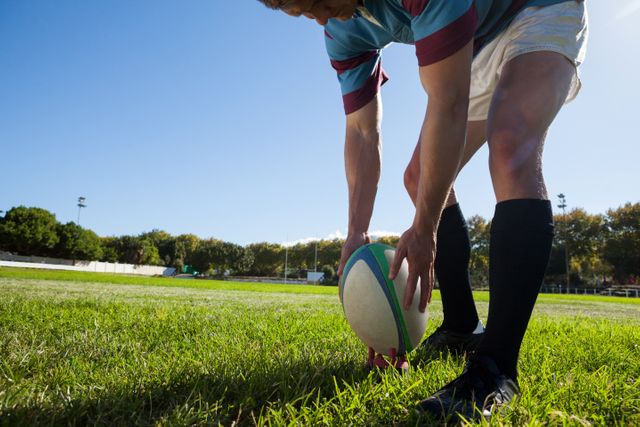 Rugby player getting ready to kick for goal on playing field against clear blue sky