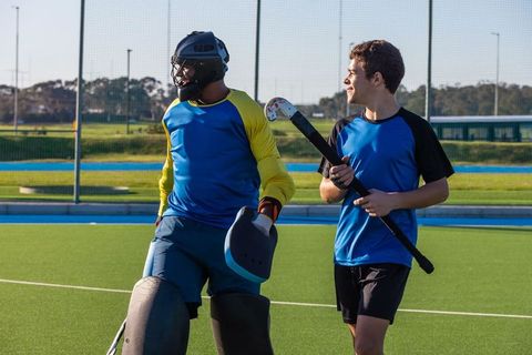 Male field hockey teammates on outdoor pitch engaging in friendly chatter