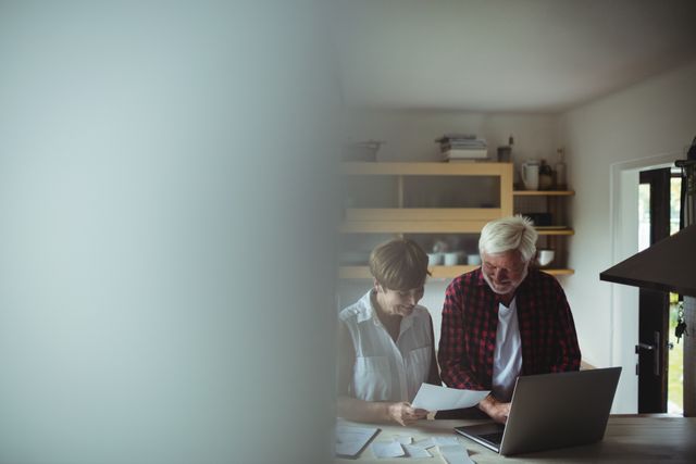Senior couple using a laptop to manage their finances at home. Ideal for articles or advertisements about online banking, financial planning for retirees, technology use among the elderly, or home-based financial management.