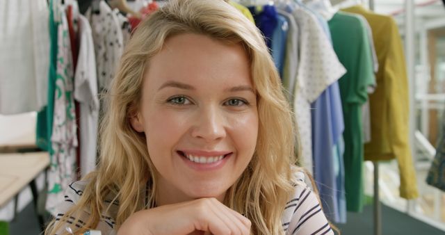 Young Caucasian woman smiles warmly in a clothing store. Her cheerful expression invites a welcoming shopping experience.