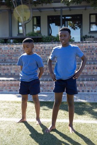 Two african american boys standing barefoot on grass in matching blue shirts