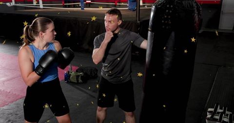 Female boxer training with coach at heavy bag in boxing gym, practicing stance and power