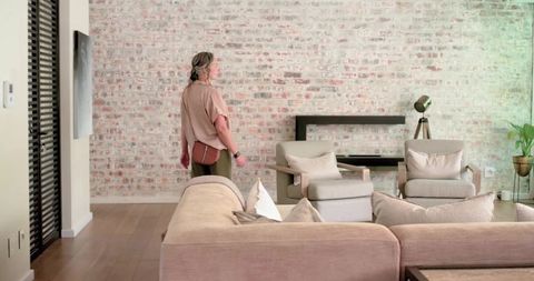 Woman standing in modern neutral living room with exposed brick wall and beige sofa