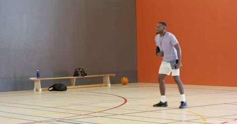 Man holding towel and phone standing on indoor basketball court near bench and ball, training focus