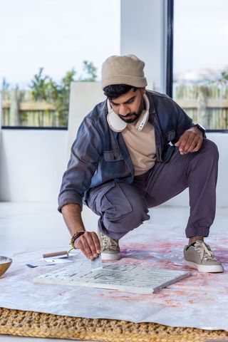 Indian artist kneeling applying textured paint with palette knife in bright modern studio