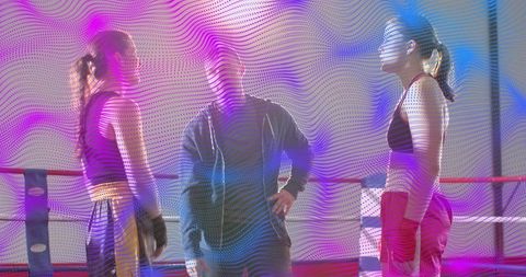 Female boxers facing off in ring with coach during sparring session under neon lights