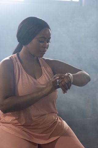 African american woman checking fitness tracker during gym rest wearing pink activewear