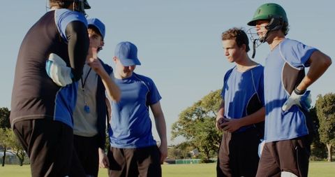 Youth baseball team huddling with coach on sunny outfield during practice and strategy talk