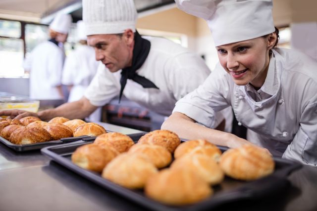 Chefs in a hotel kitchen preparing fresh kaiser rolls. Ideal for use in culinary blogs, cooking tutorials, hospitality industry promotions, and bakery advertisements. Highlights teamwork and professional culinary skills.