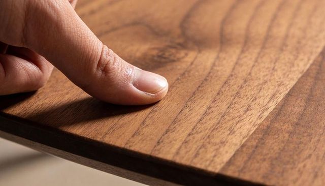 Finger gliding across finished walnut panel showing rich grain texture and warm brown tone