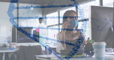 Masked asian woman talking on phone at desk in open-plan biotech office with dna overlay