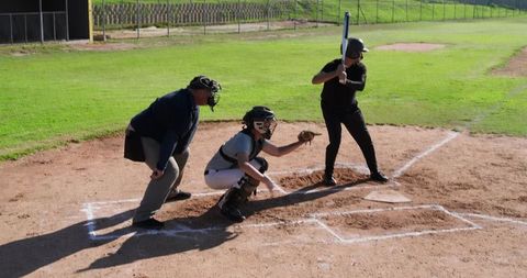Youth baseball batter catcher umpire crouching at home plate on sunny community field