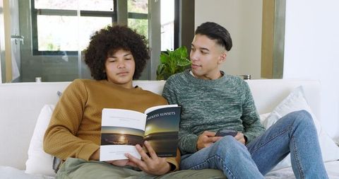 Diverse friends relaxing with book and smartphone on cozy sofa
