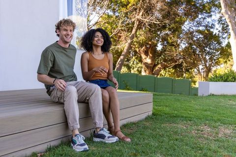 Young couple relaxing on raised wooden deck in sunny backyard with lush green lawn