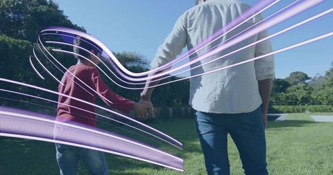 Parent and child walking hand-in-hand on sunny lawn with purple light trails