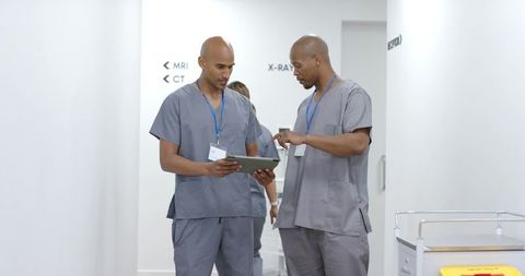 African american clinicians reviewing tablet in hospital corridor, demonstrating teamwork