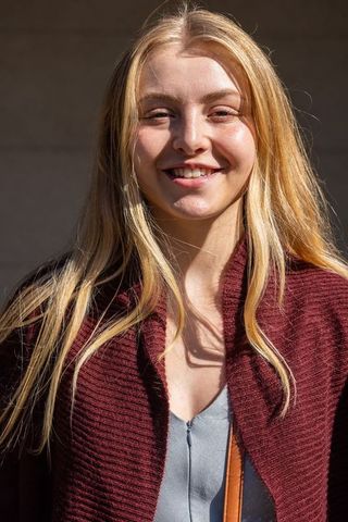 Sunlit young woman smiling in maroon cardigan outdoor portrait headshot