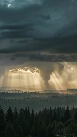 Vertical storm video of funnel cloud descending over forest with sunbeams piercing clouds