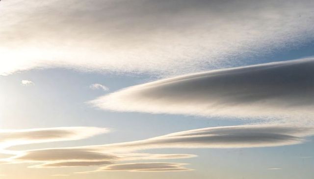Sunlit lenticular cloud bands flowing across sky with low-sun veil over horizon