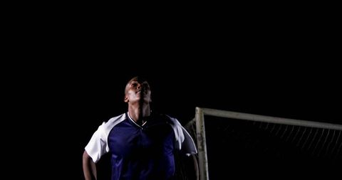 Soccer player gazing under stadium lights at night near goalpost and net