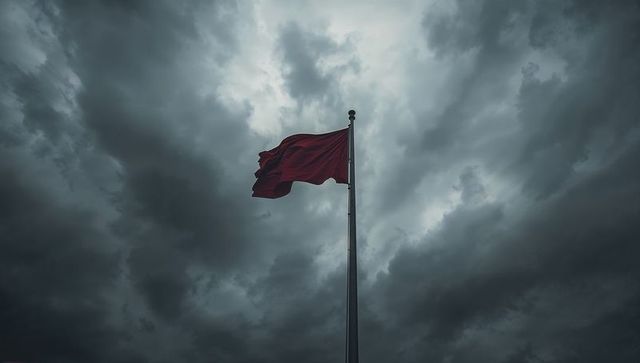 Solitary red flag flying on tall pole against dramatic storm clouds and gusty wind
