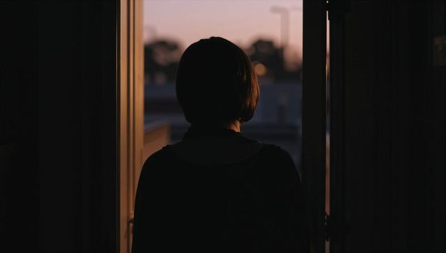 Contemplative woman silhouette standing in doorway gazing at dusk sky with warm backlight