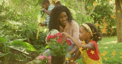 Mother teaching daughter gardening in sunny backyard planting and touching pink blooms