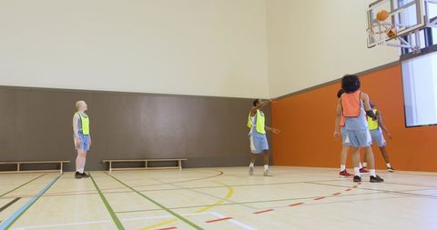 Diverse male basketball players contesting rebound on indoor court wearing neon pinnies