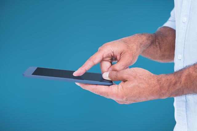 Man's hands using tablet against blue background. Suitable for technology, digital communication, and professional work contexts. Great for illustrating themes such as remote work, online learning, and social media interaction.