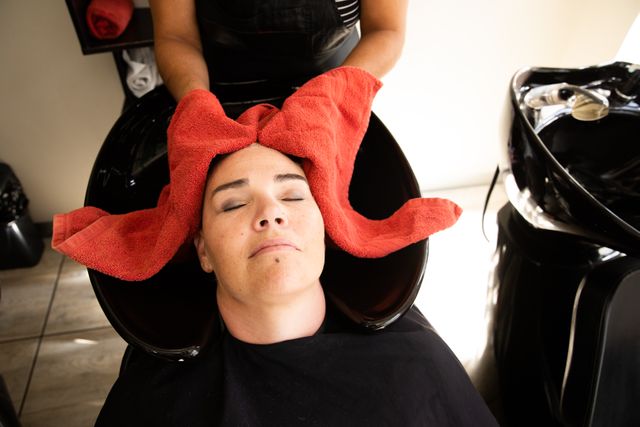 High angle front view of a middle aged biracial female hairdresser and a young Caucasian woman having her hair dried with a towel, in a hair salon